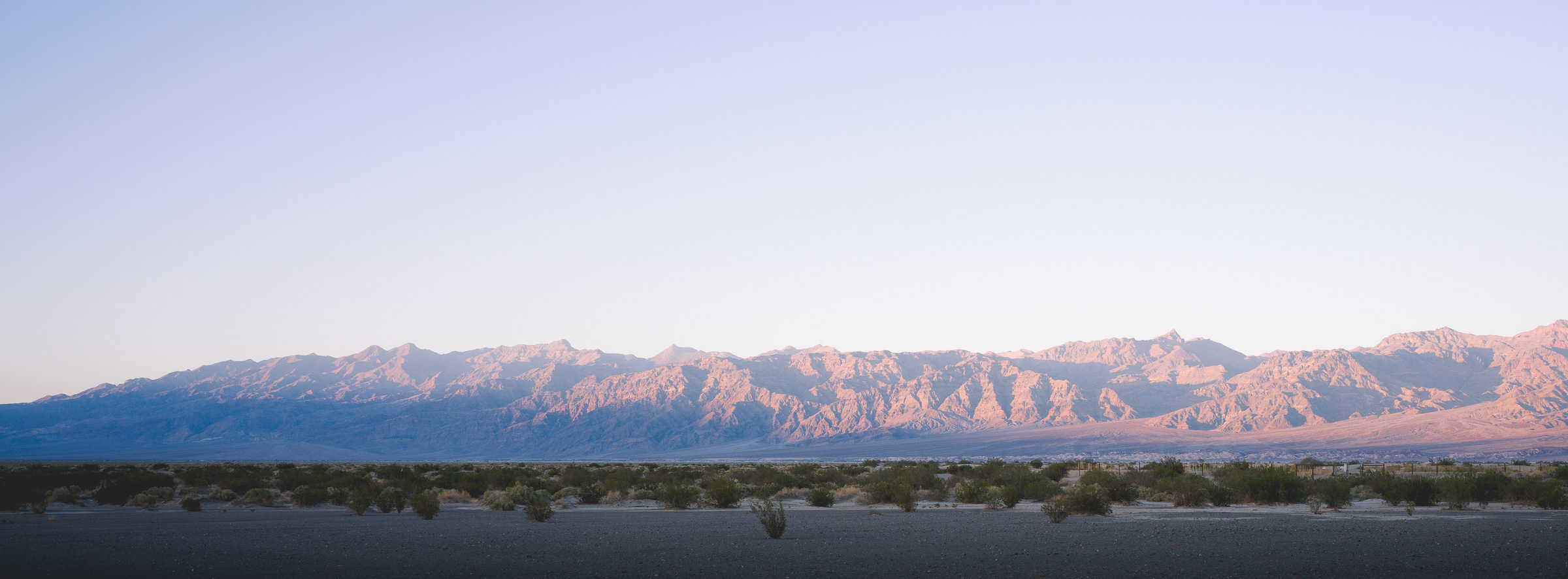 Panoramic desert mountain range glowing pink at sunrise