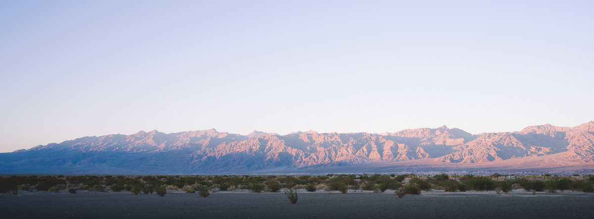 Dawn alpenglow paints a distant mountain range above the desert floor.