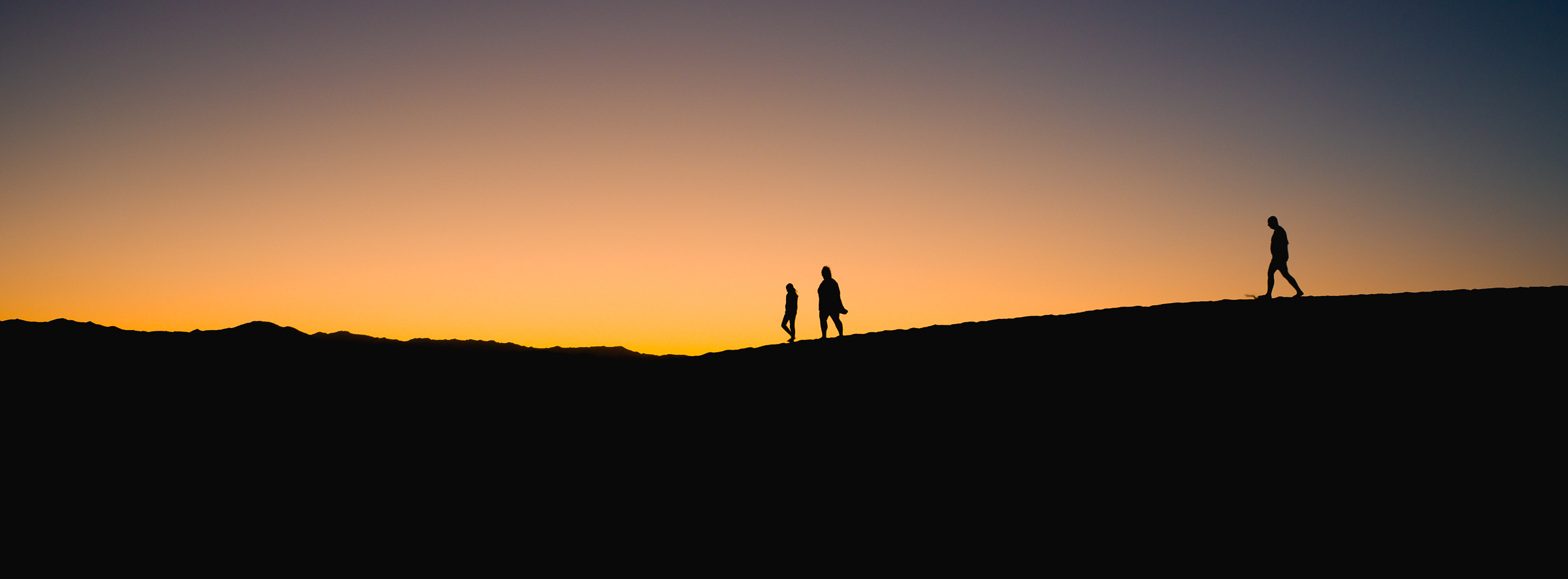 Three silhouettes walk a dune ridge against a blazing desert sunset.