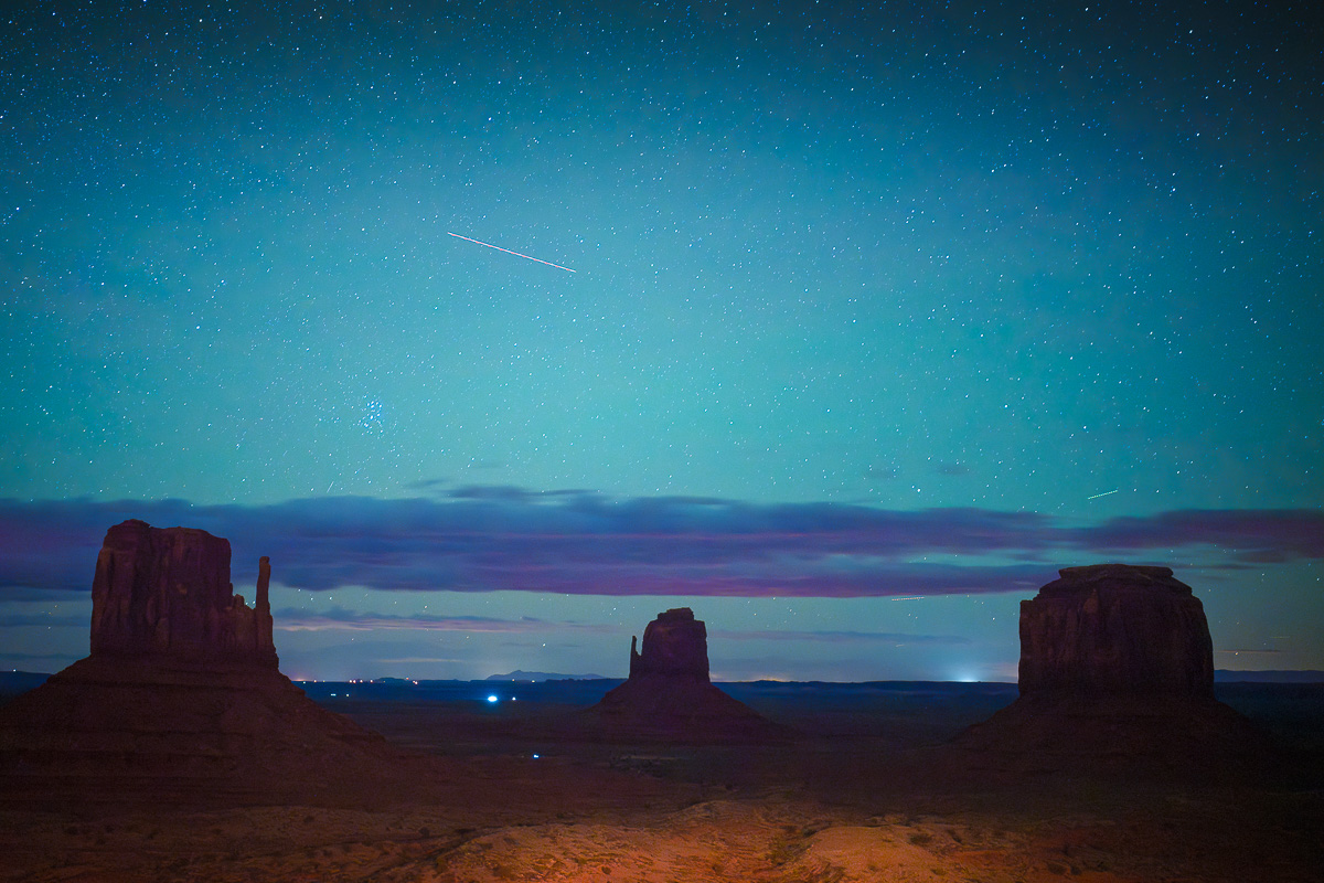 Monument Valley's mittens stand sentinel beneath a star-filled turquoise night sky.