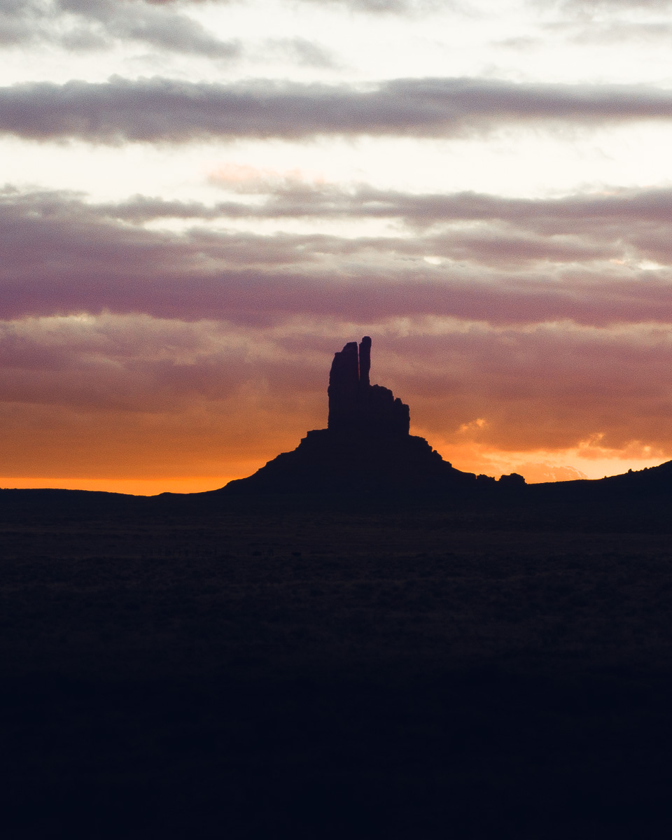 A desert butte stands silhouetted against a molten orange and violet sky.