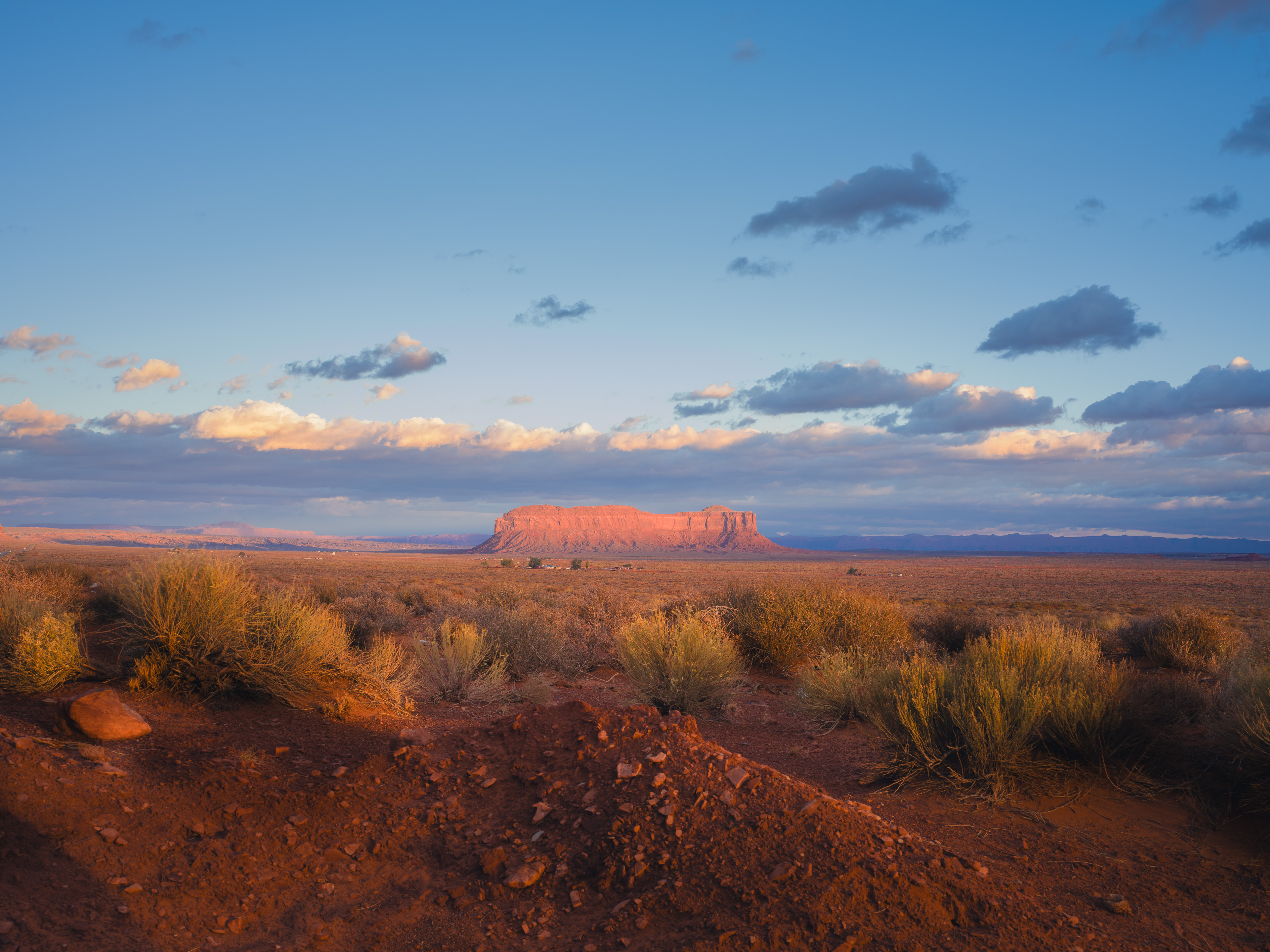 A crimson mesa glows at sunset across the vast Navajo desert plain.