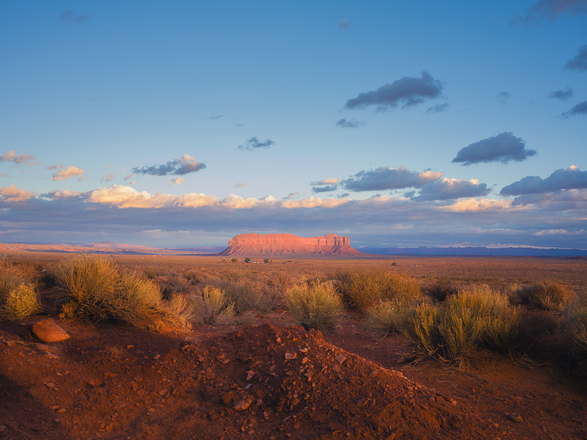 A crimson mesa glows at sunset across the vast Navajo desert plain.