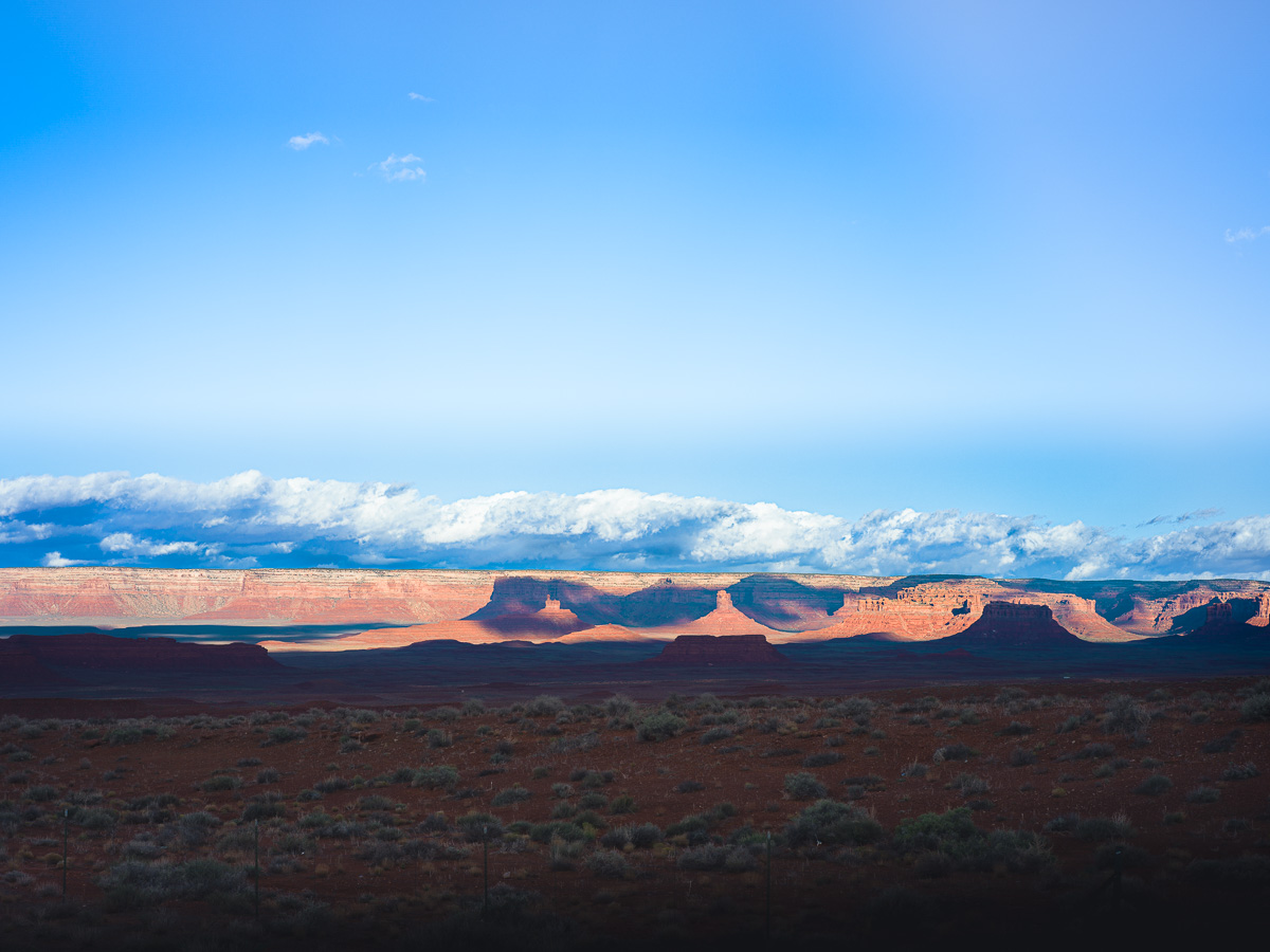 Red mesas rise from shadowed desert floor beneath an endless Utah sky.
