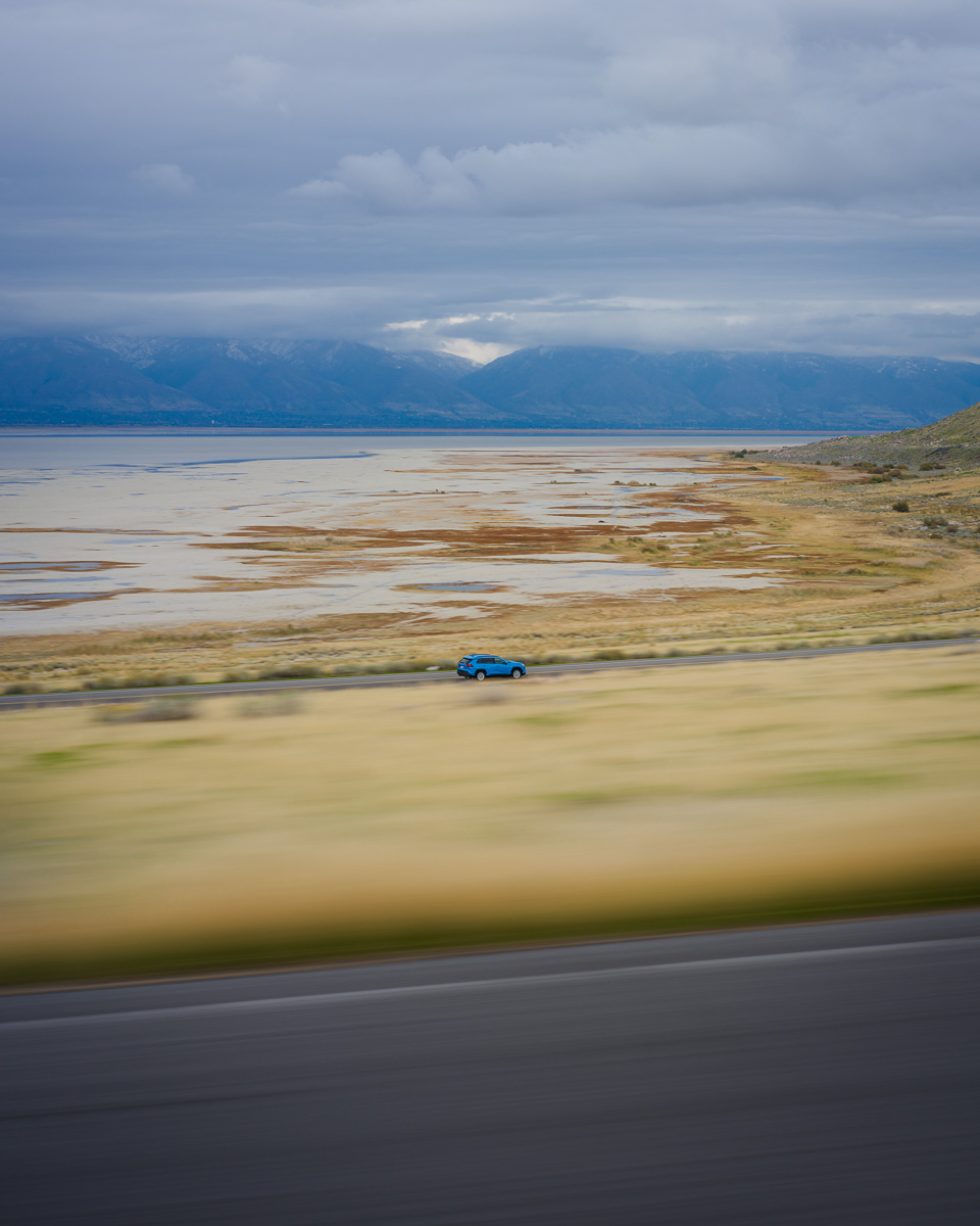 A lone car races past the vast salt flats under brooding skies.