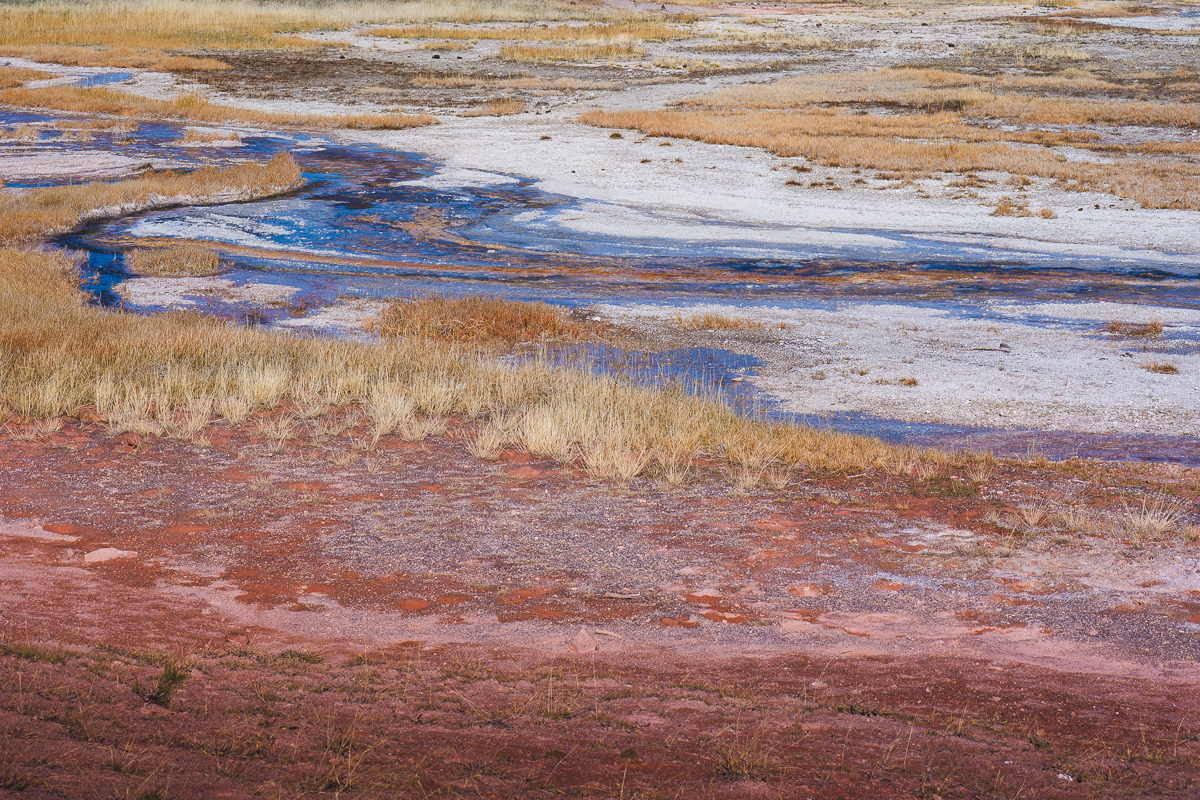 Mineral-stained earth and blue rivulets pattern a geothermal basin floor.