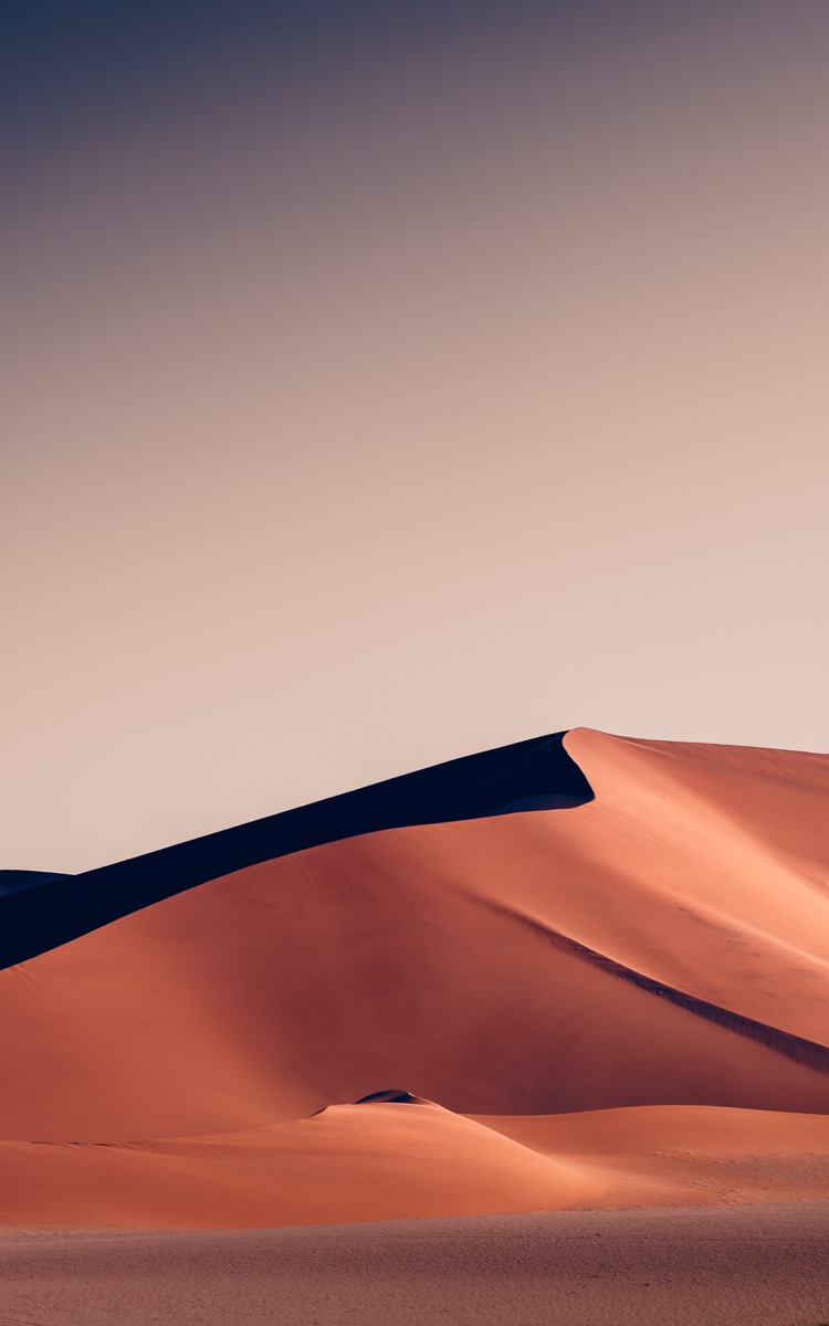 Crimson dunes carve sharp ridgelines beneath a vast twilight sky.